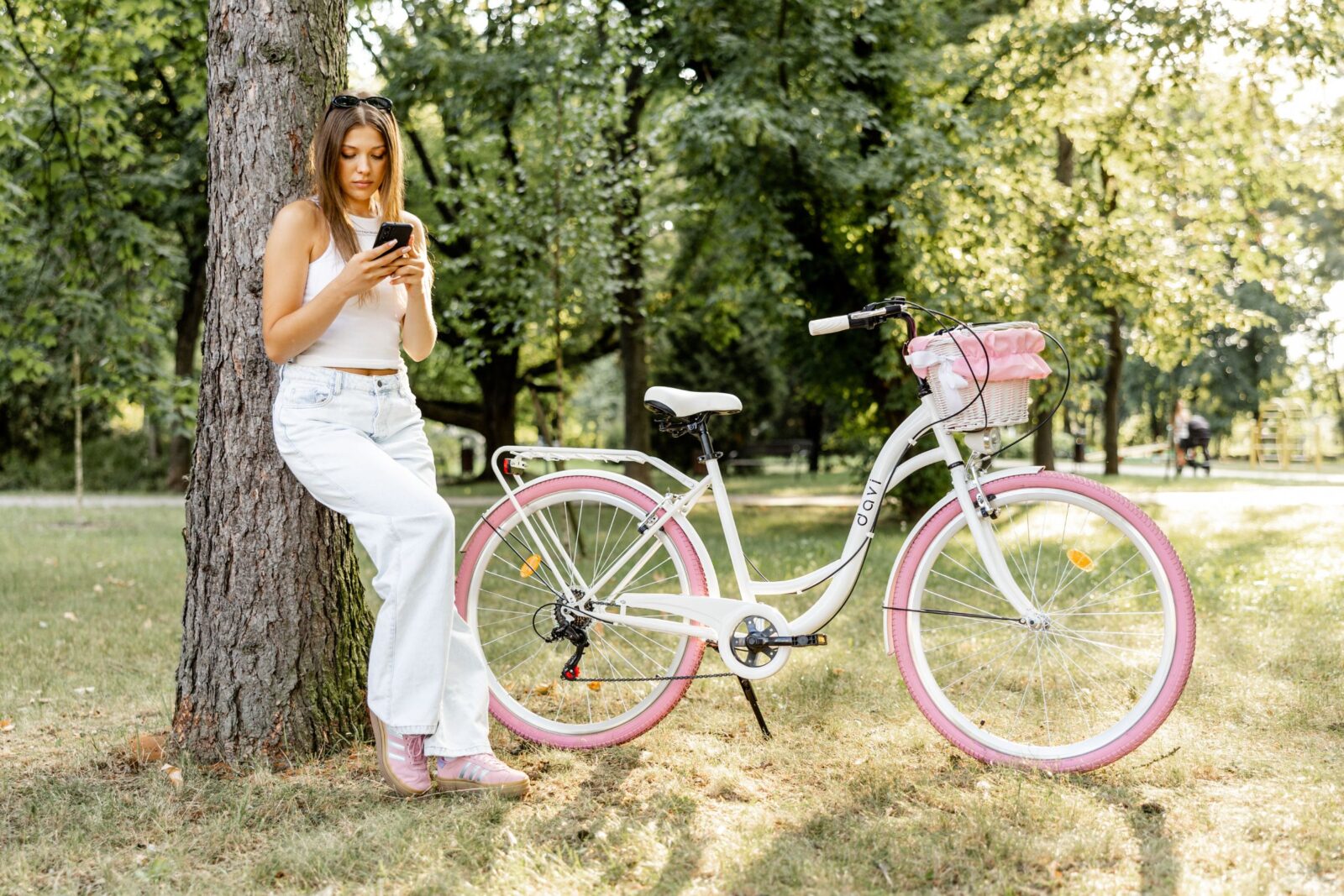 Kvinna vid cykel, tittar på mobil i park.