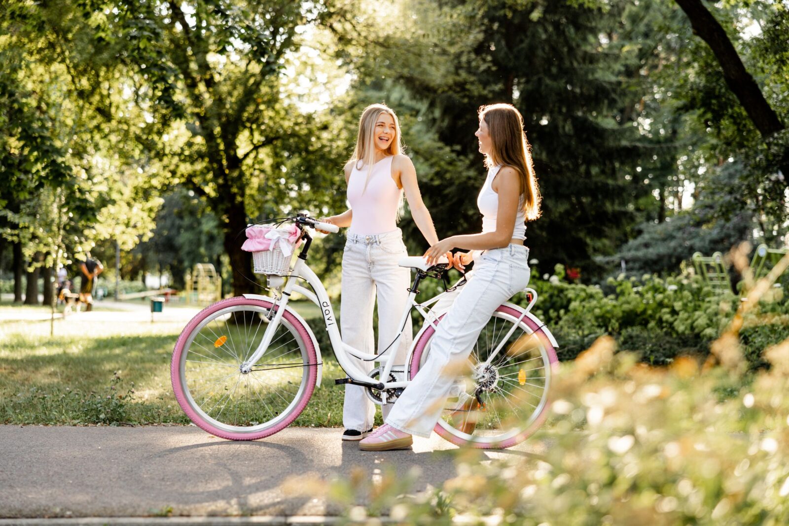 Två kvinnor med cykel i solig park