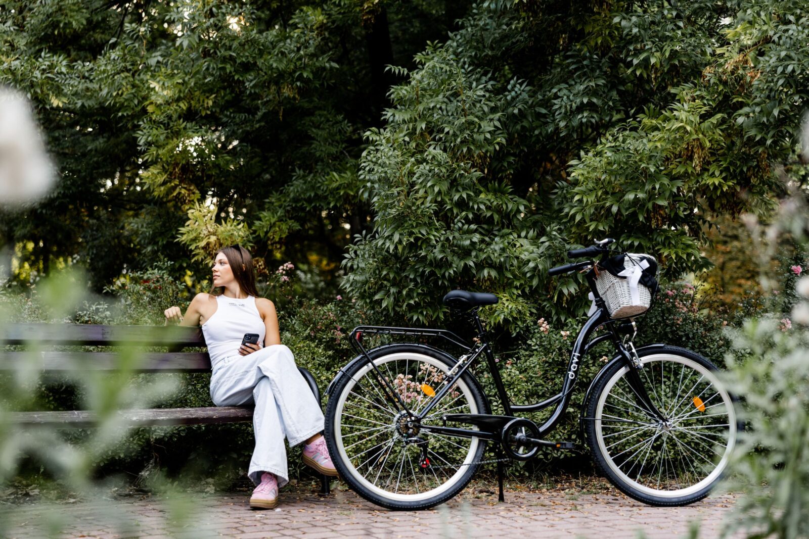 Kvinna sitter på bänk med cykel i parken.