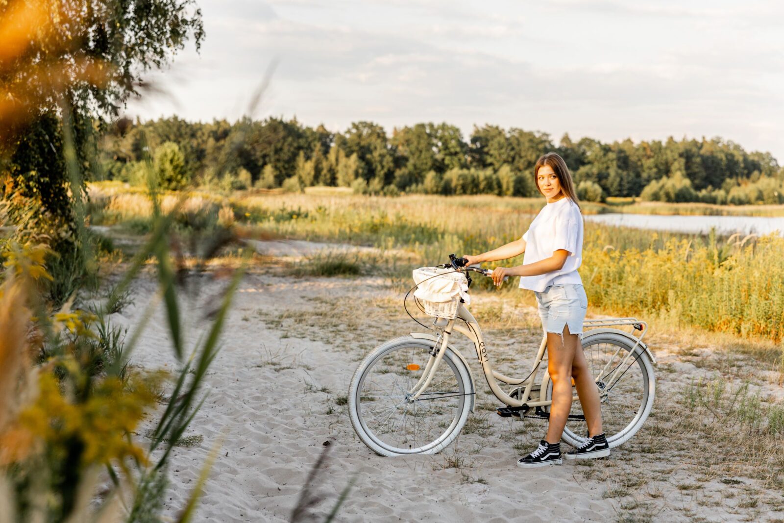 Kvinna med cykel på sandstig vid sjö.