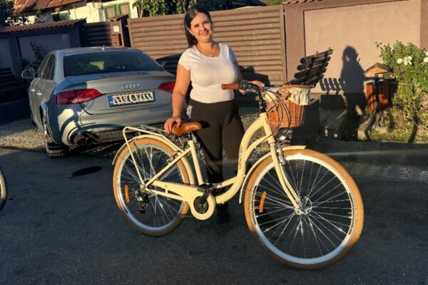 Kvinna med cykel framför bil i solsken.