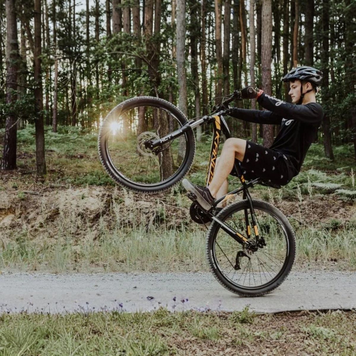 Mladý cyklista robí wheelie v lese.